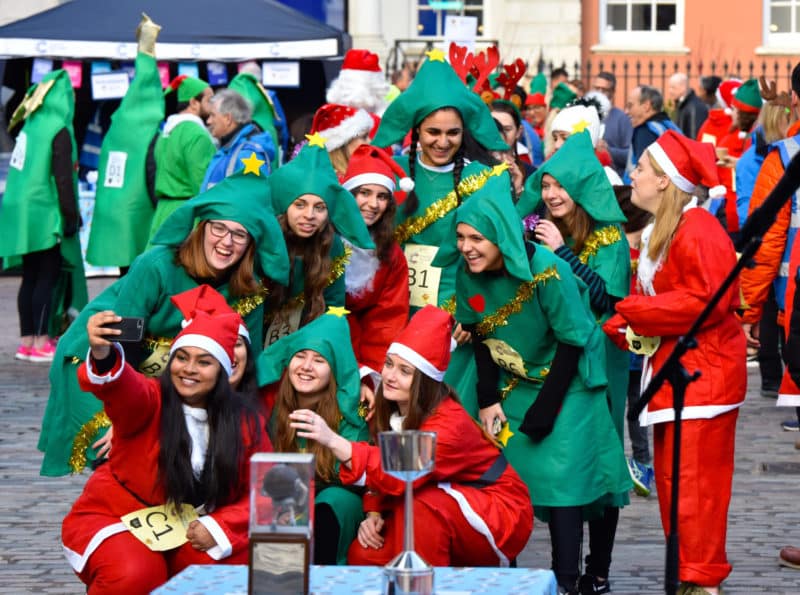 A group of ten women, dressed in Santa costumes and green elf costumes, pose for a photo after the Great Christmas Pudding Race.