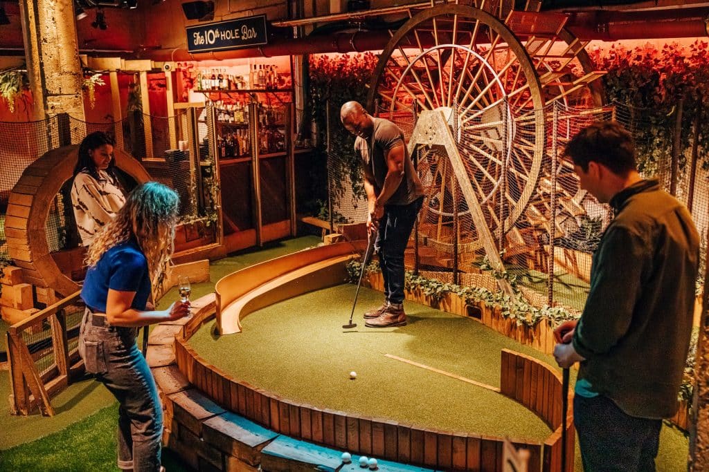 Four people on a double date watch as one of them putts his ball on the crazy golf green.
