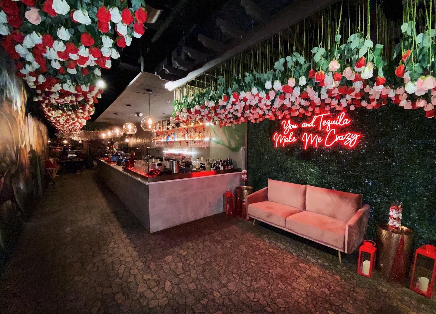 A bar with red and white roses hanging from the ceiling, plus slate features and a red neon sign on the wall.
