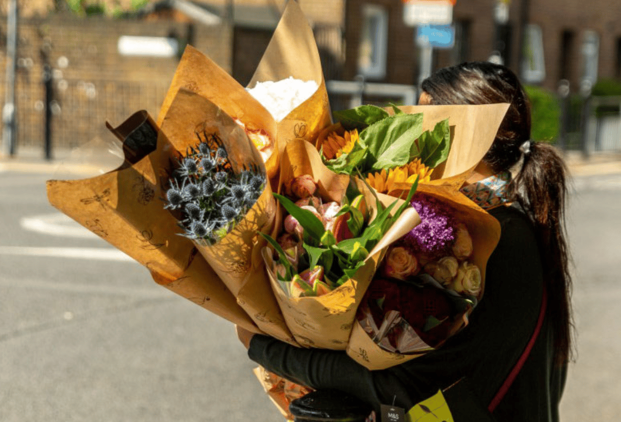 A woman carries several bouquets of flowers – peonies, roses, sunflowers and more – across the street.