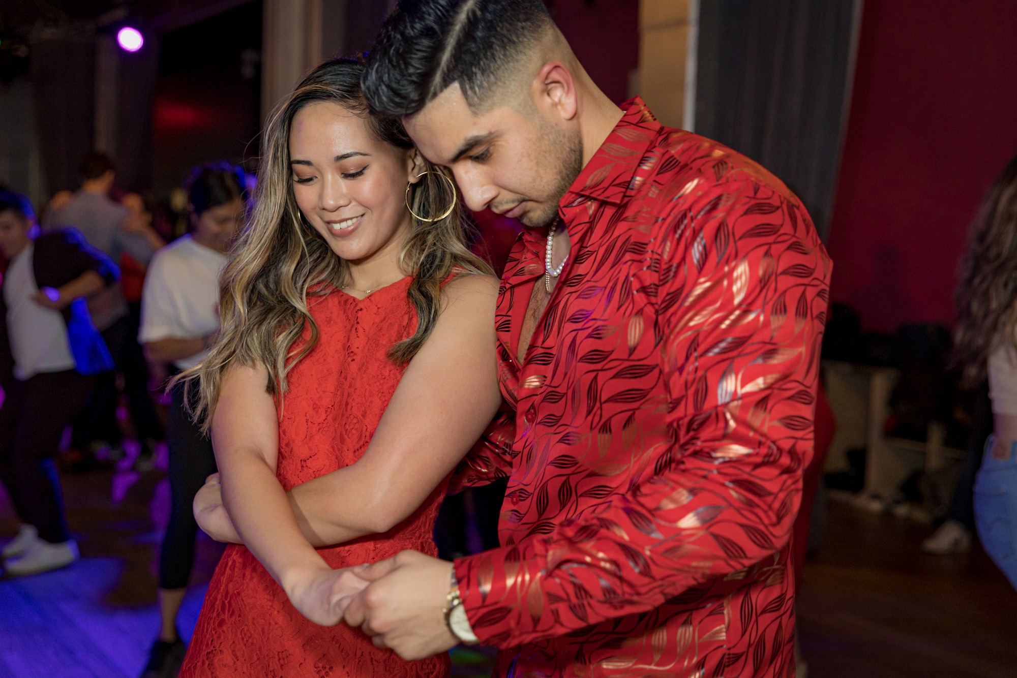 A man and woman, both dressed in red, hold hands and move into their next salsa position.
