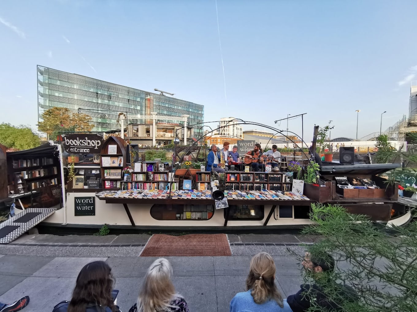 A book barge on Regent's Canal with books on display and musicians playing on the deck.