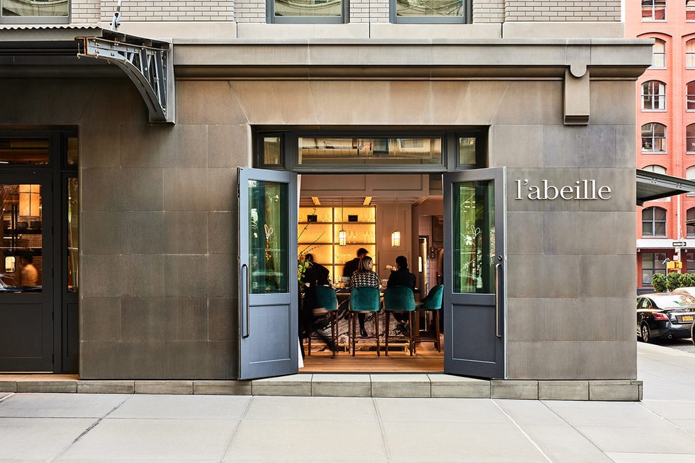 The gray stone exterior of l’abeille restaurant, with the doors thrown open to the warm interior.