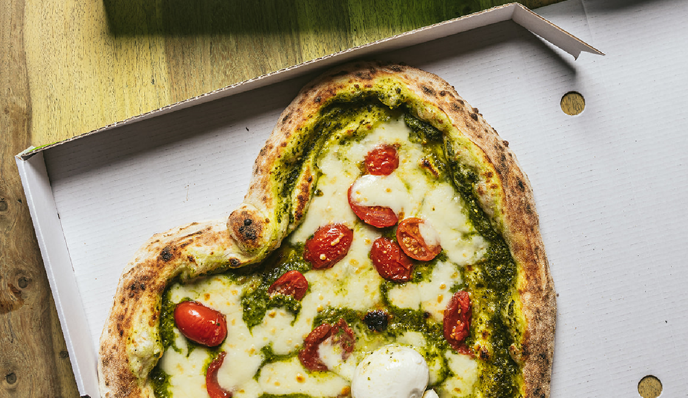 A heart-shaped sourdough pizza topped with pesto, burrata and plum tomatoes.
