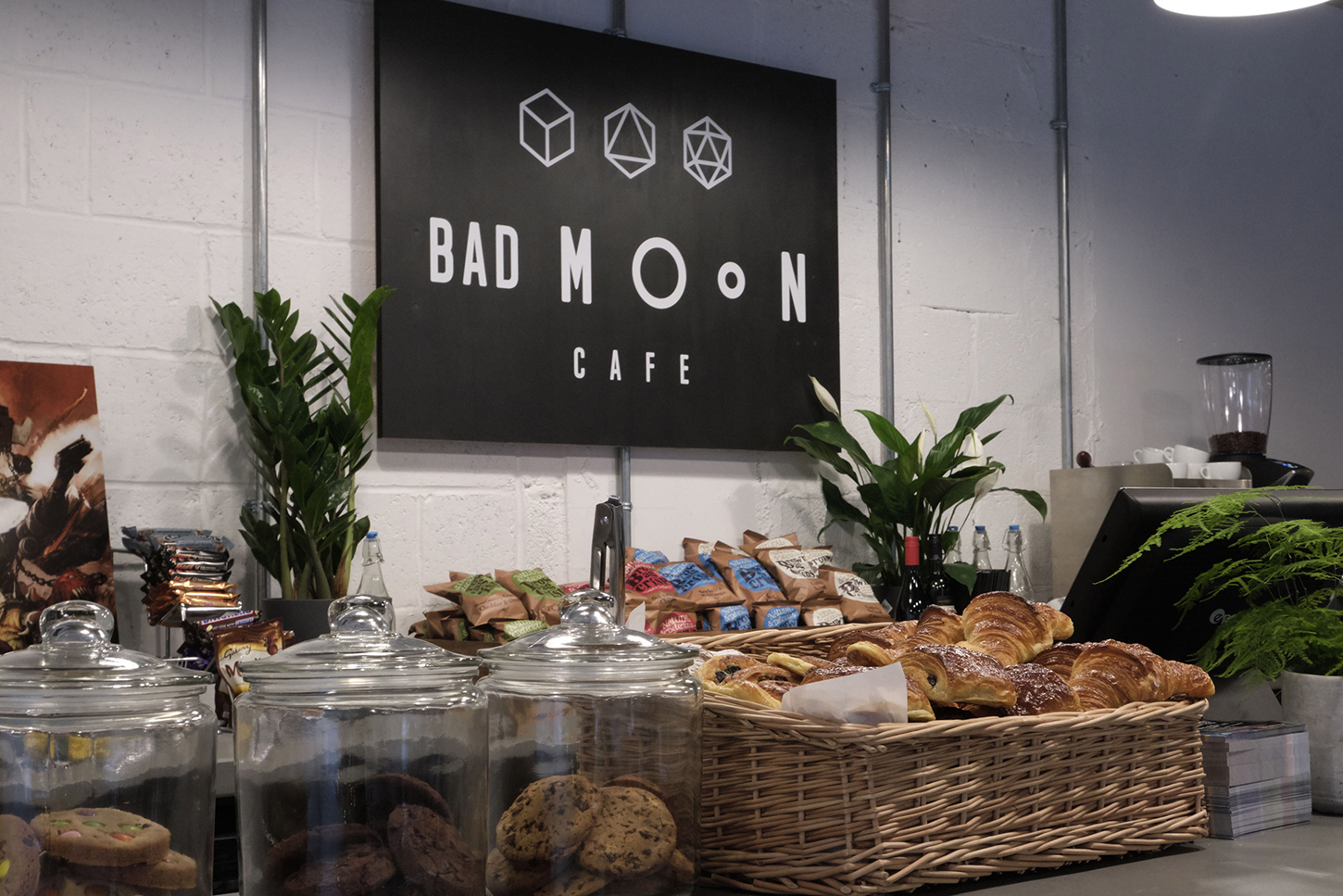 The counter at the Bad Moon Cafe, complete with a geometric sign, small plants and a basket of croissants in front.