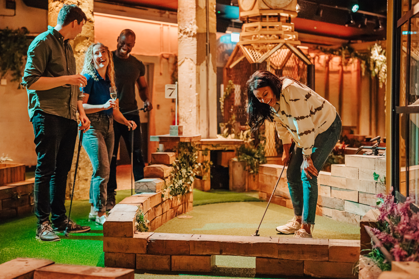 Two men and two women laugh with one another on the crazy golf course, as one of the women putts her ball.