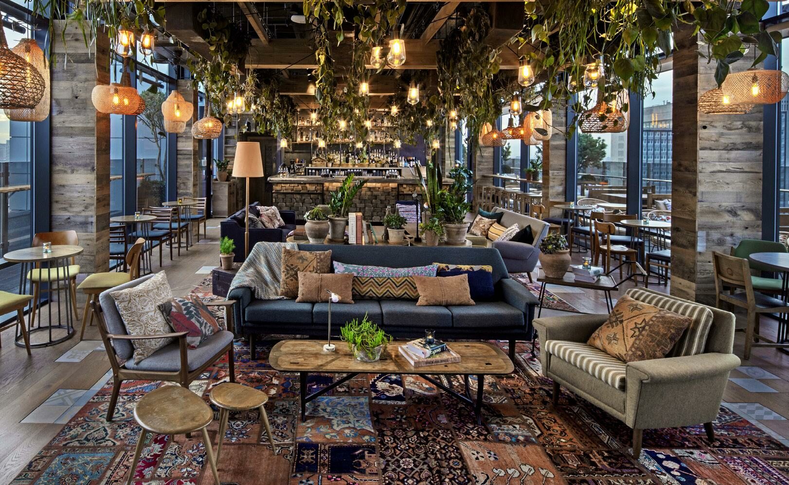 An indoor/outdoor rooftop bar with plenty of tables, comfortable sofas and chairs, patterned rugs and pillows and hanging vines.