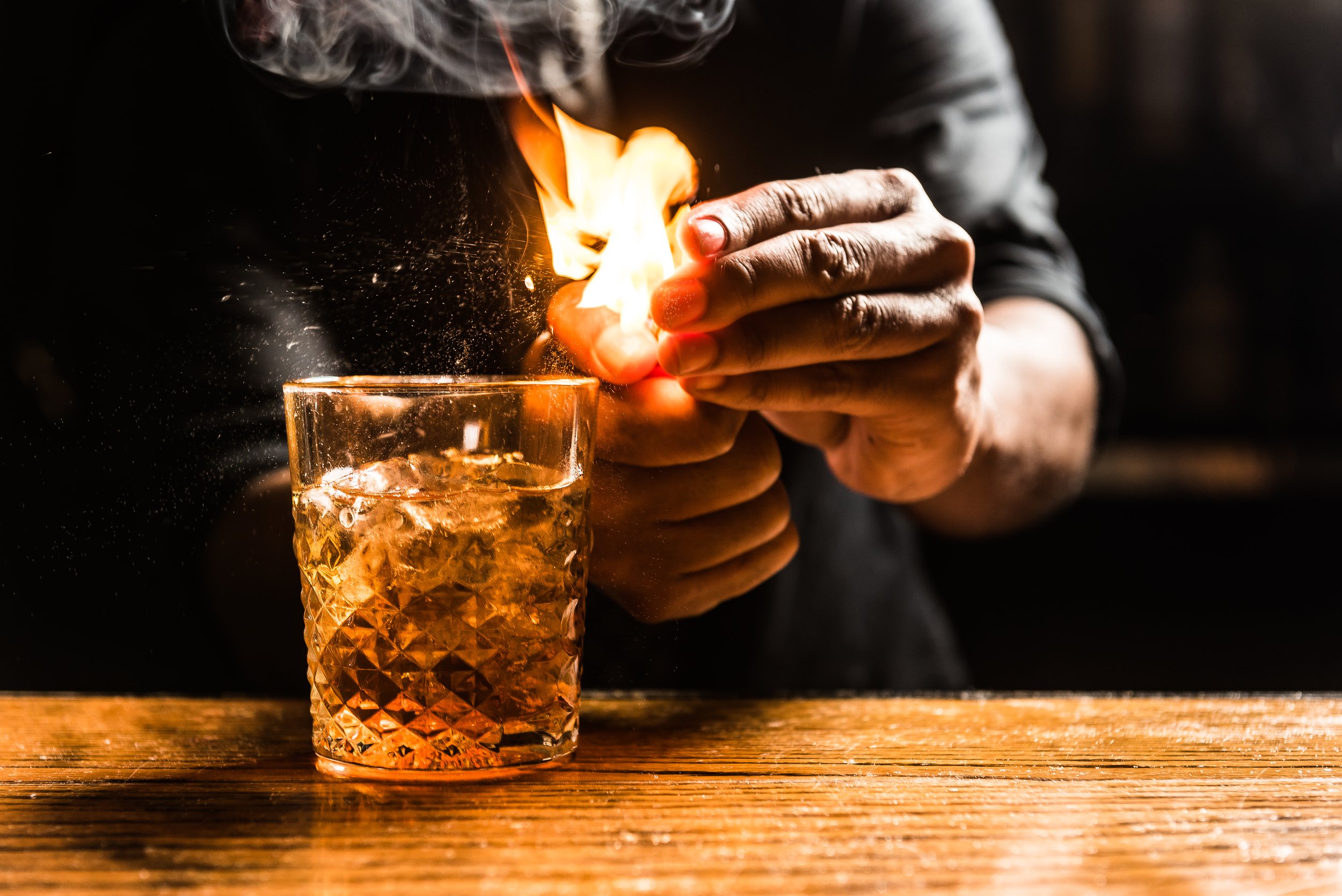 A bartender lights a match to create a flaming cocktail at Bar Charley.