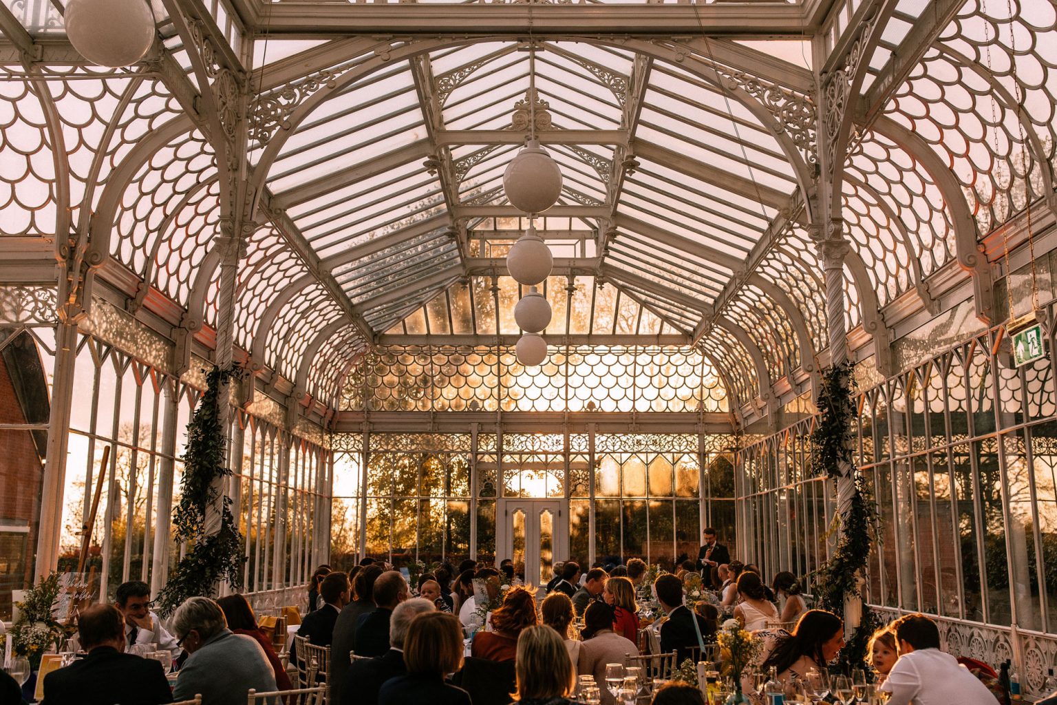 The interior of a Victorian glass conservatory, filled with people for a reception.