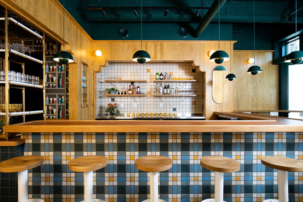 A modern bar featuring blue, yellow and white tile and light wooden surfaces.