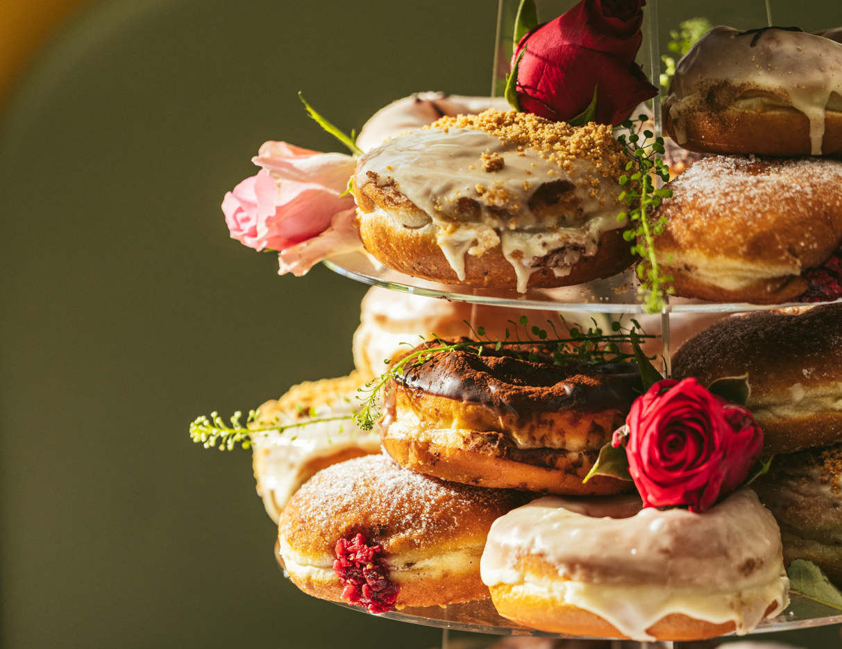 A doughnut tower with tiers of iced and sugar-dusted doughnuts, adorned with real pink roses.