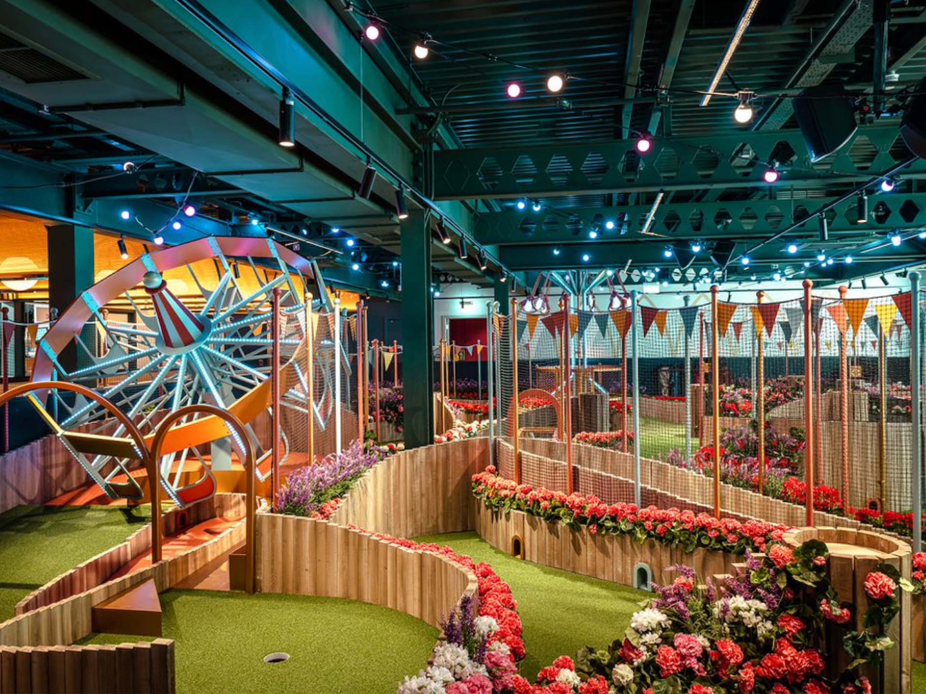 An indoor crazy golf course featuring a colourful spinning wheel and flowers lining the green.