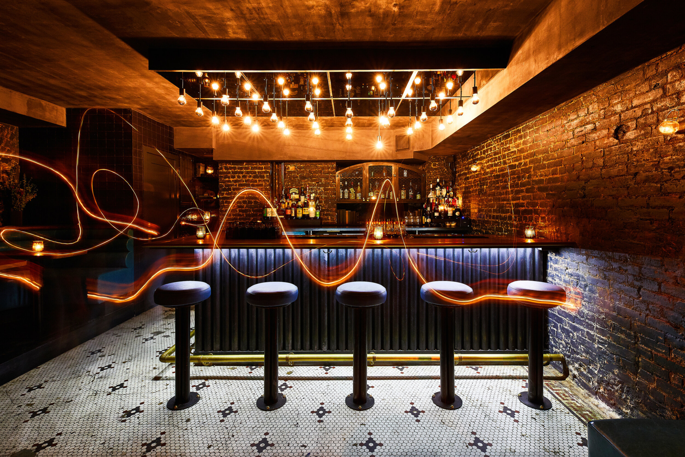 An underground bar featuring exposed brick and a ceiling installation of hanging light bulbs.