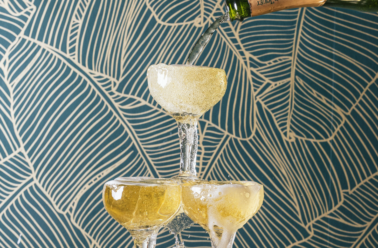 A champagne tower of three coupe glasses overflowing with bubbling Perrier-Jouët.