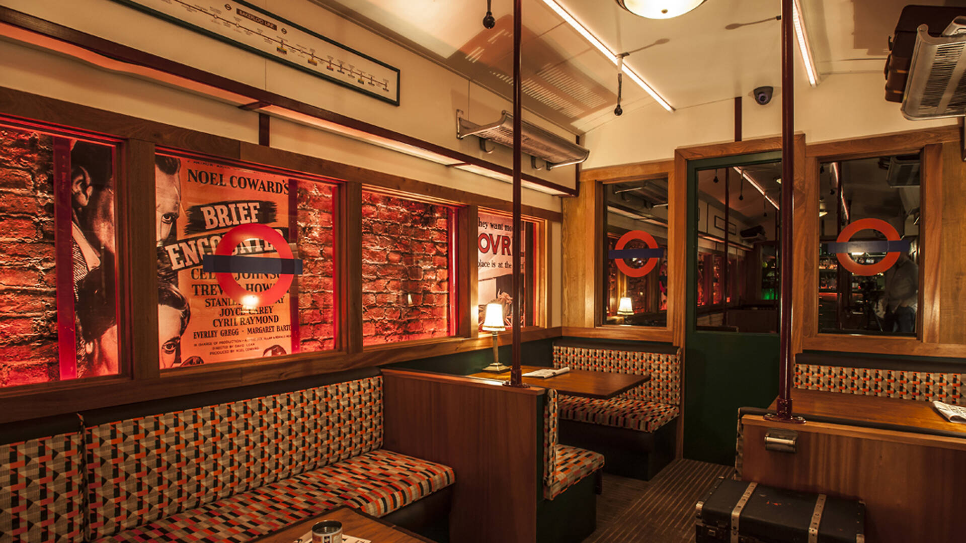Three restaurant booths, upholstered to look like tube seats, sit tucked against the wall of a red-lit speakeasy.