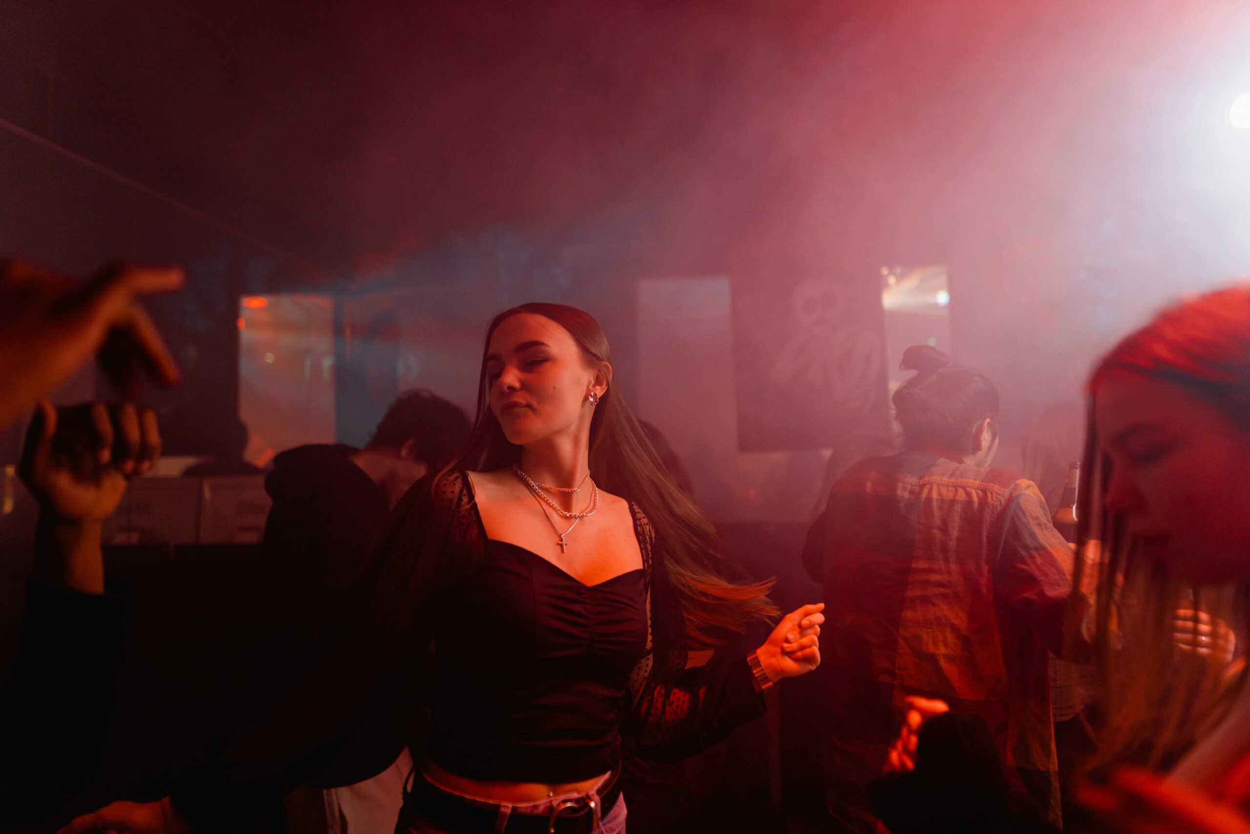 A girl in a black top dances in a bar with smoke and purple lights.