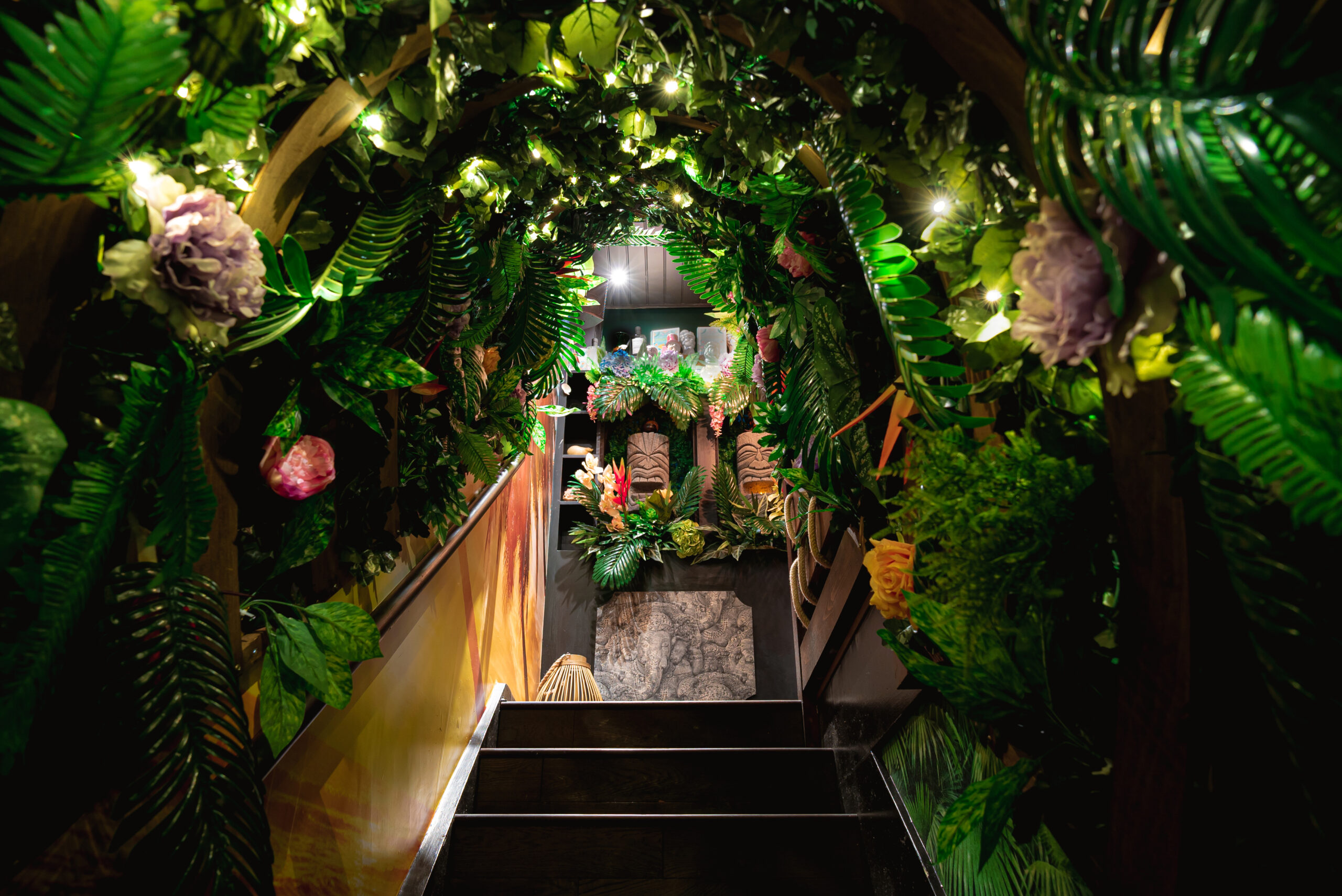 Stairs lead to the second floor of Laki Kane’s tiki bar; the stairwell itself is canopied in lush tropical plants and flowers.