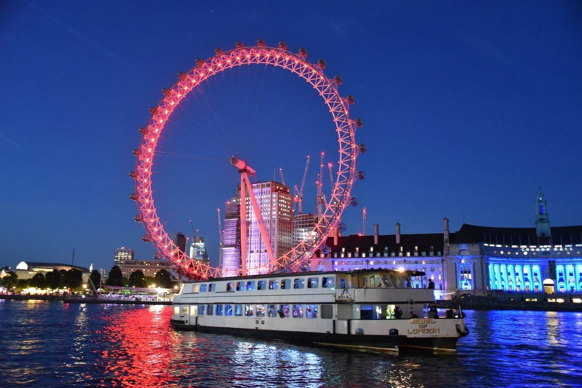'Jewel of London' Party boat cruising along the Thames in front of an illuminated London Eye