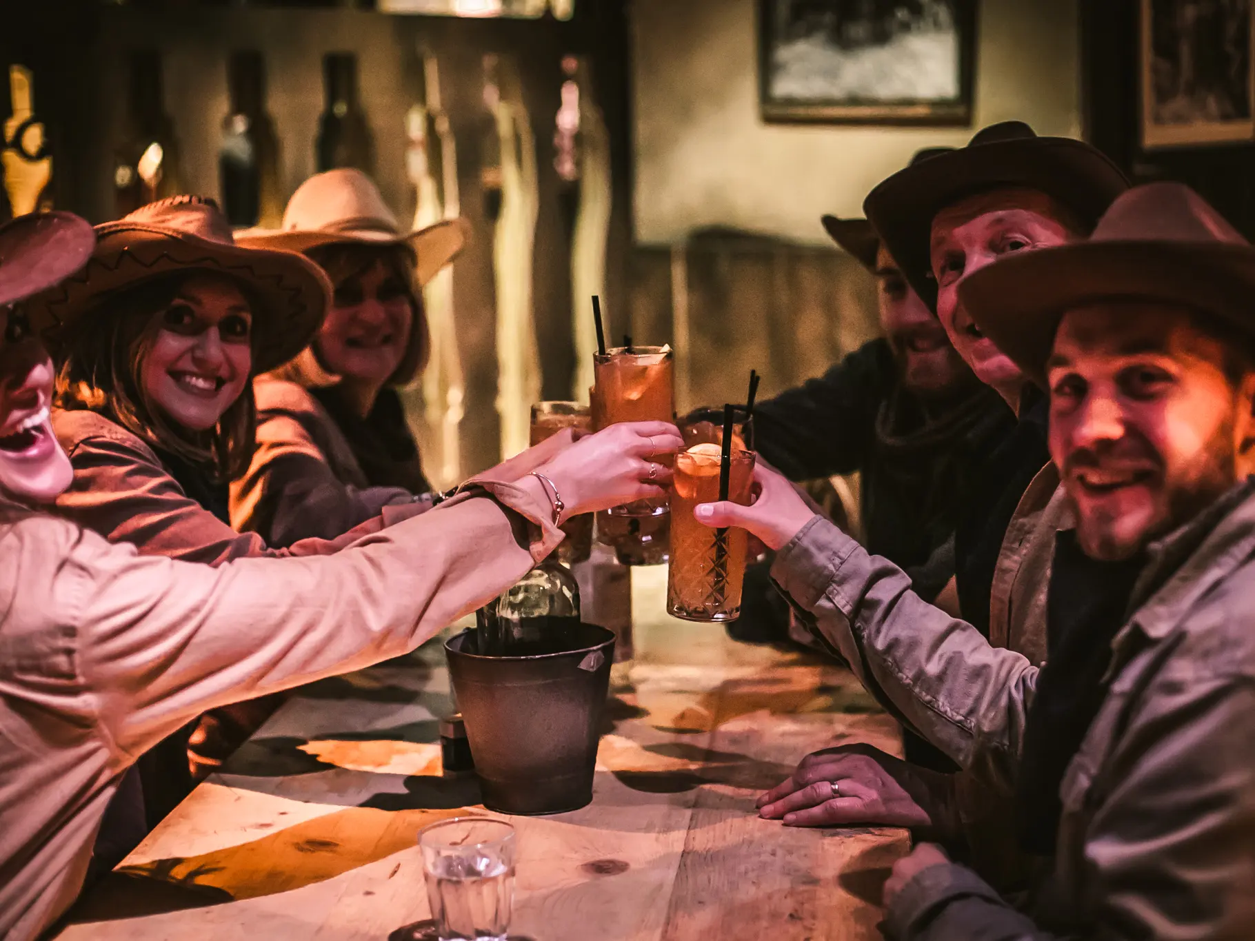 A group wearing cowboy hats sit at a card table covered in drinks