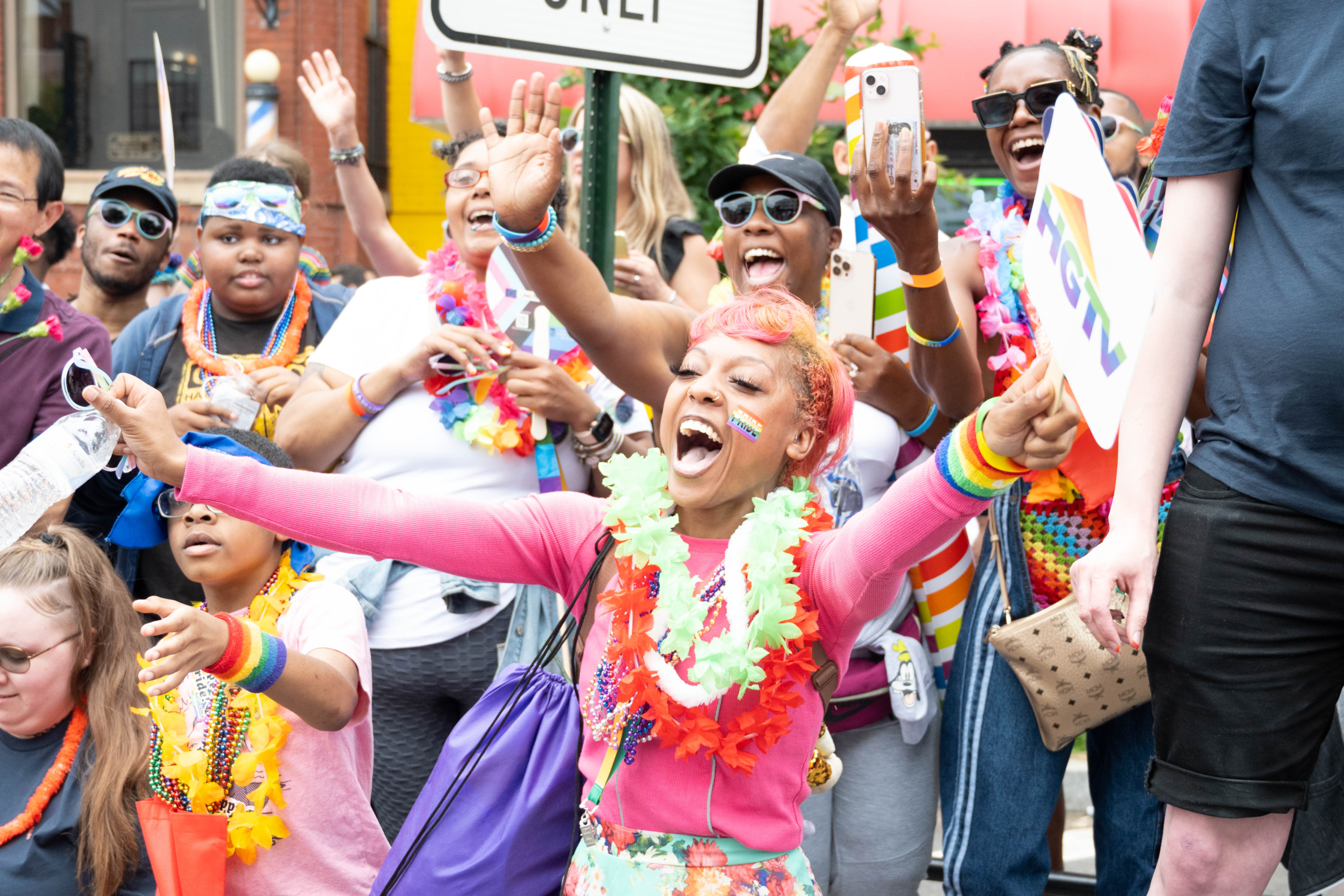 People dressed in bright colours and rainbow accessories hold signs and cheer at the DC Pride Parade.