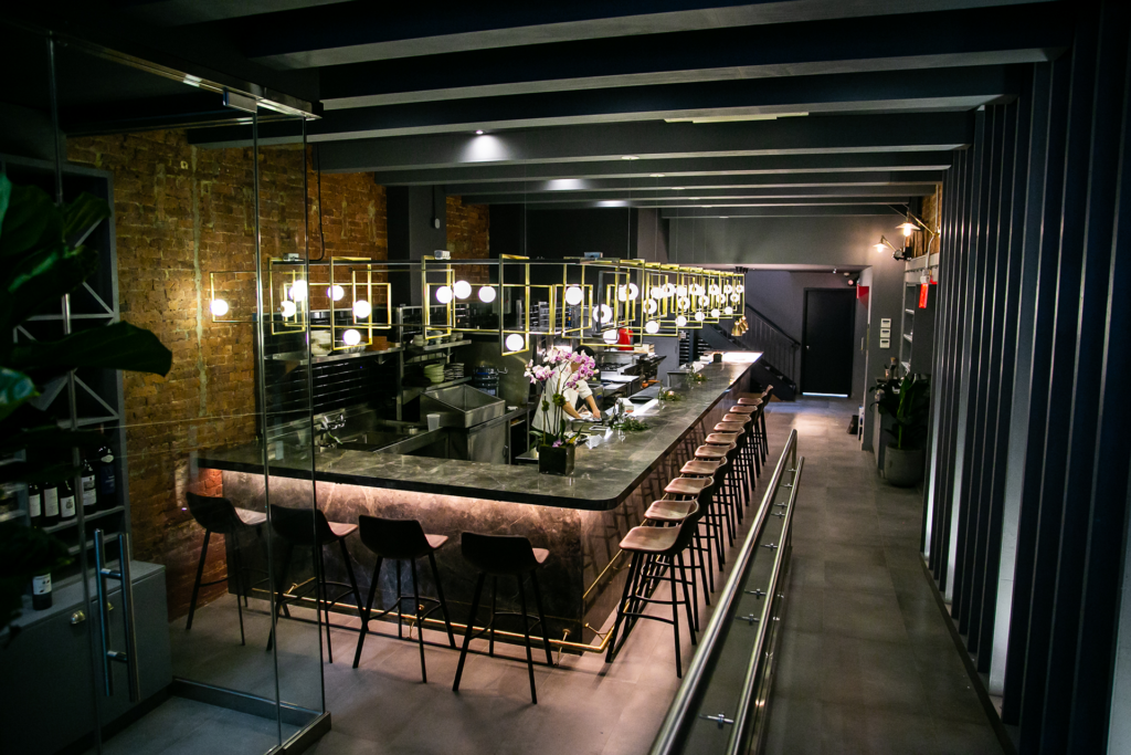 A modern bar with high stools, a marble countertop, ambient lighting, and exposed brick walls, creating a chic, cozy atmosphere. 