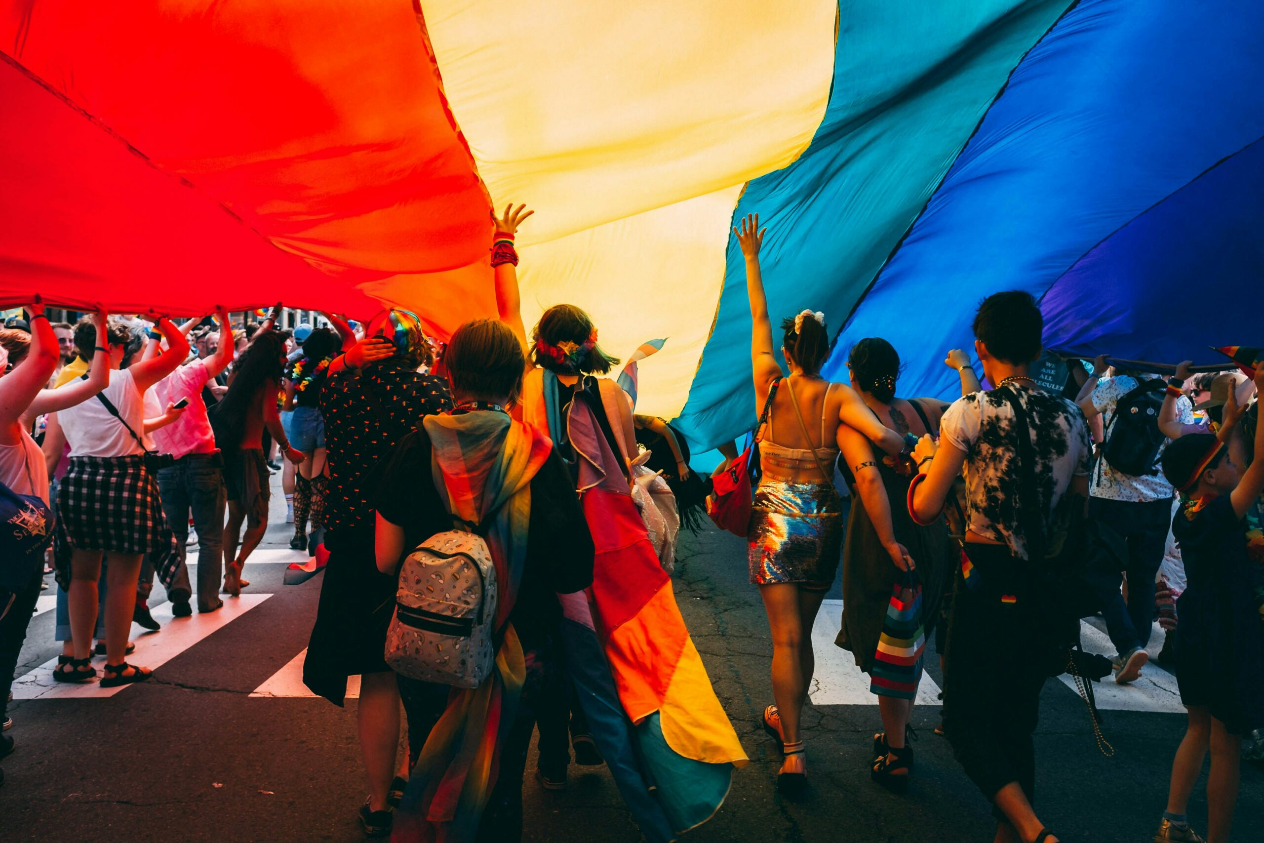 people under a rainbow flag on a pride parade